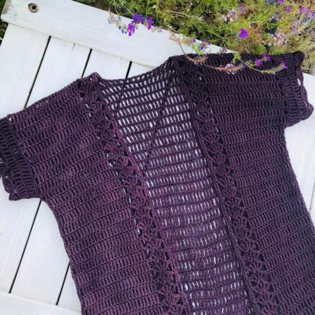 Purple crochet cardigan with short sleeves laid flat on a white background.