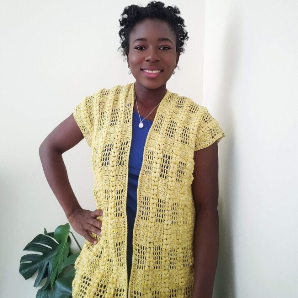 Woman wearing a long yellow lacy crochet cardigan with short sleeves.