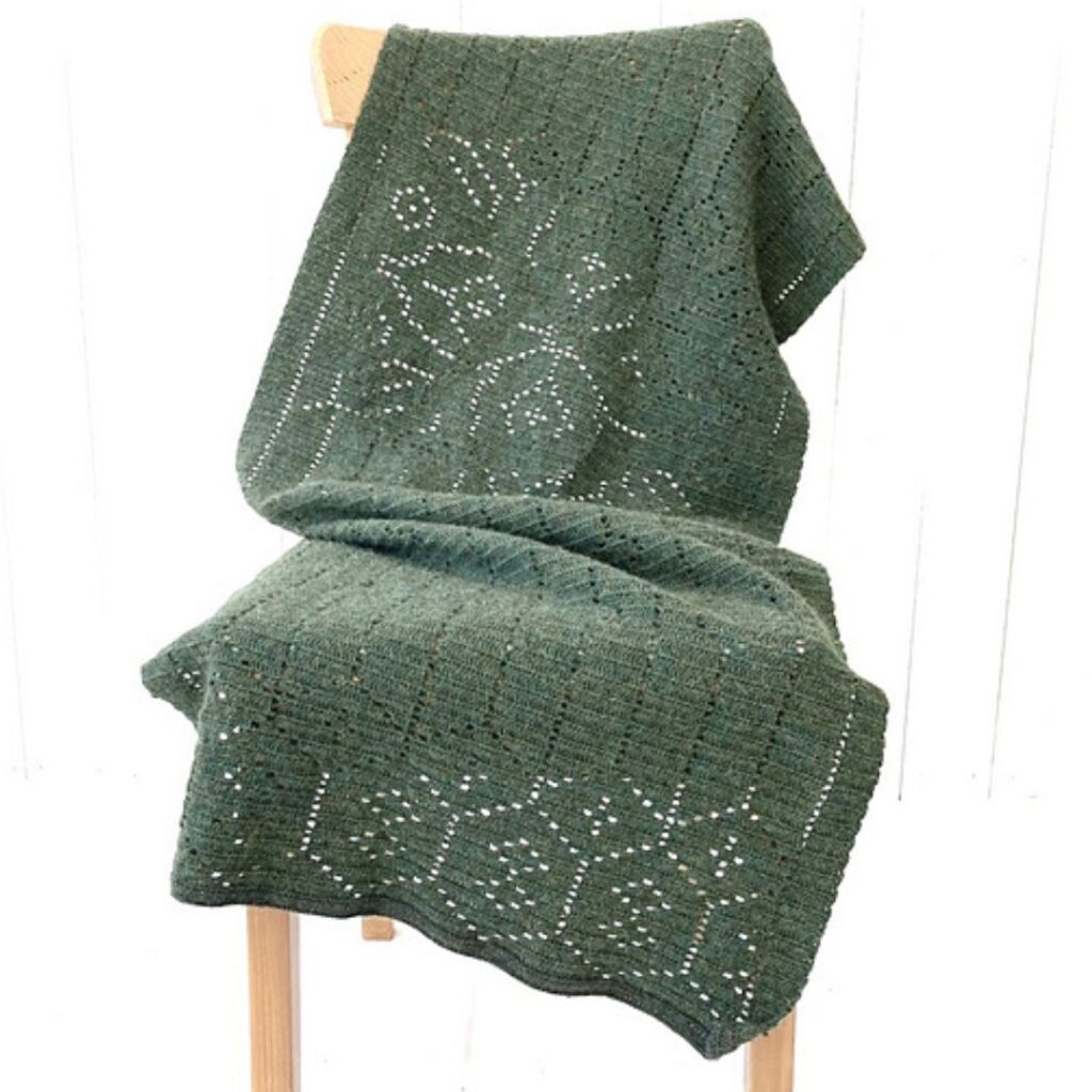 Dark green lacy crochet rectangle shaped shawl draped across a wooden chair.