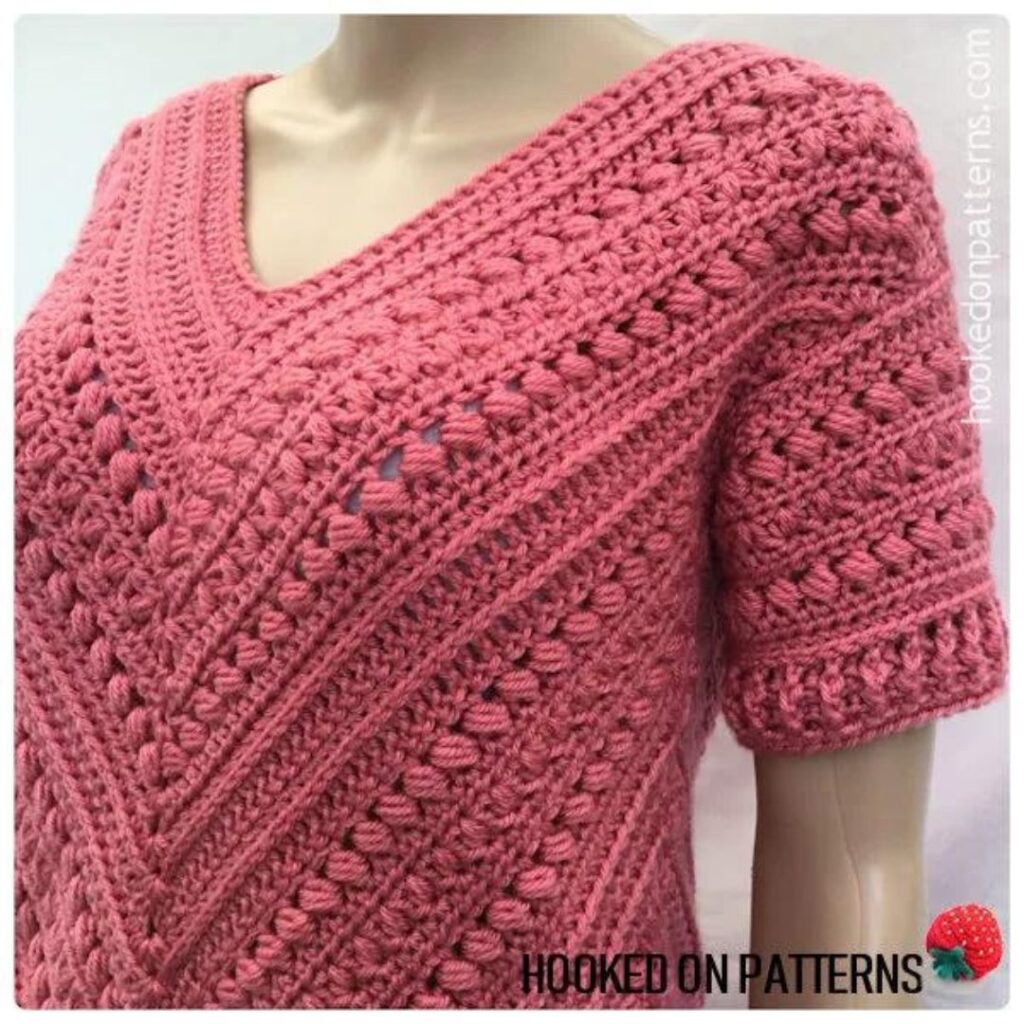 Deep pink textured crochet tunic with short sleeves on a plastic mannequin.