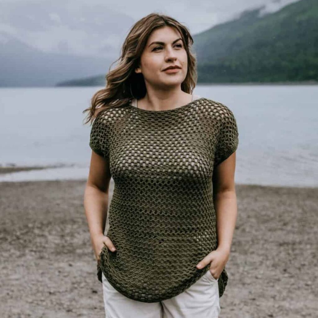 Woman wearing a dark green crochet mesh t-shirt over a white tank top. The mesh is tight and the holes are small.