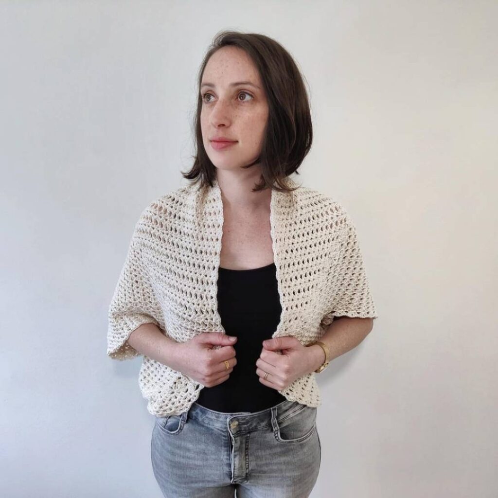 Woman wearing a white crochet shrug over her shoulders.