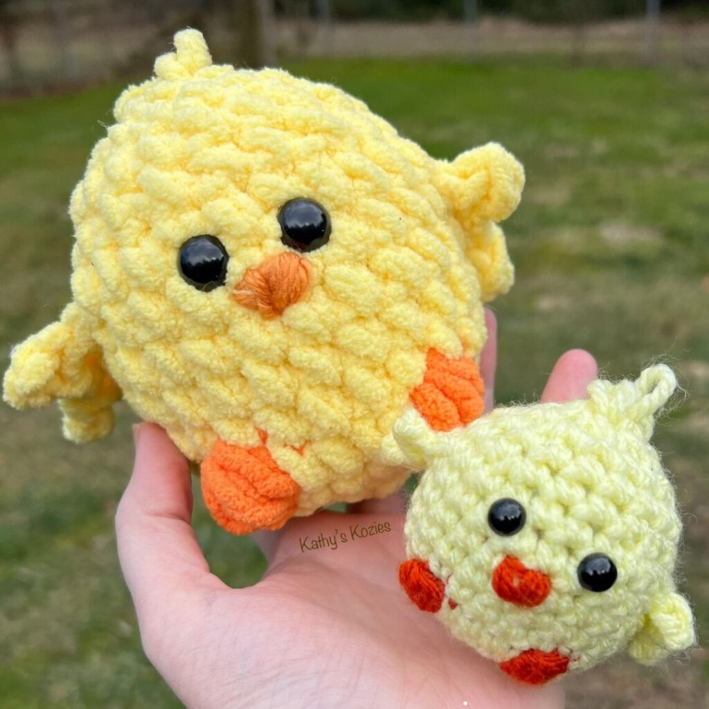 Two yellow crochet chicks held in the palm of a hand. One is larger than the other and is crocheted with a soft chenille yarn.