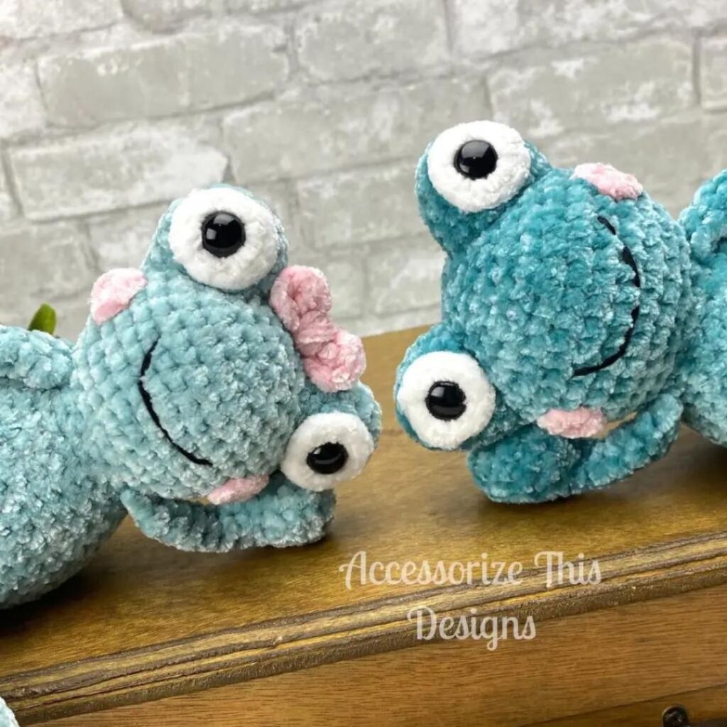 Two green crocheted frog plushies leaning into frame from either side. One has a pink bow on her head.