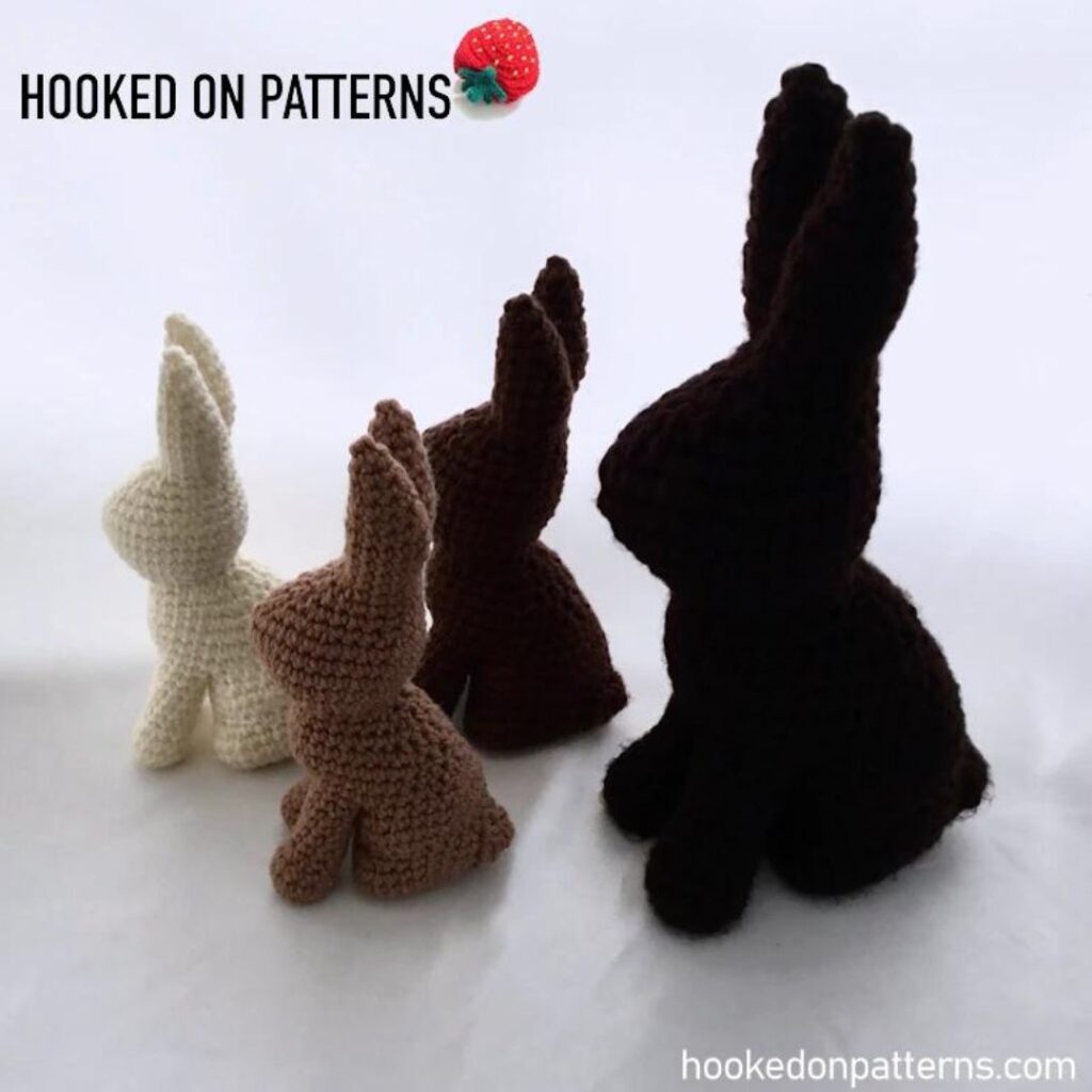 Four crochet chocolate bunnies in varying shades of brown. The bunny furthest to the right is larger and softer than the rest.