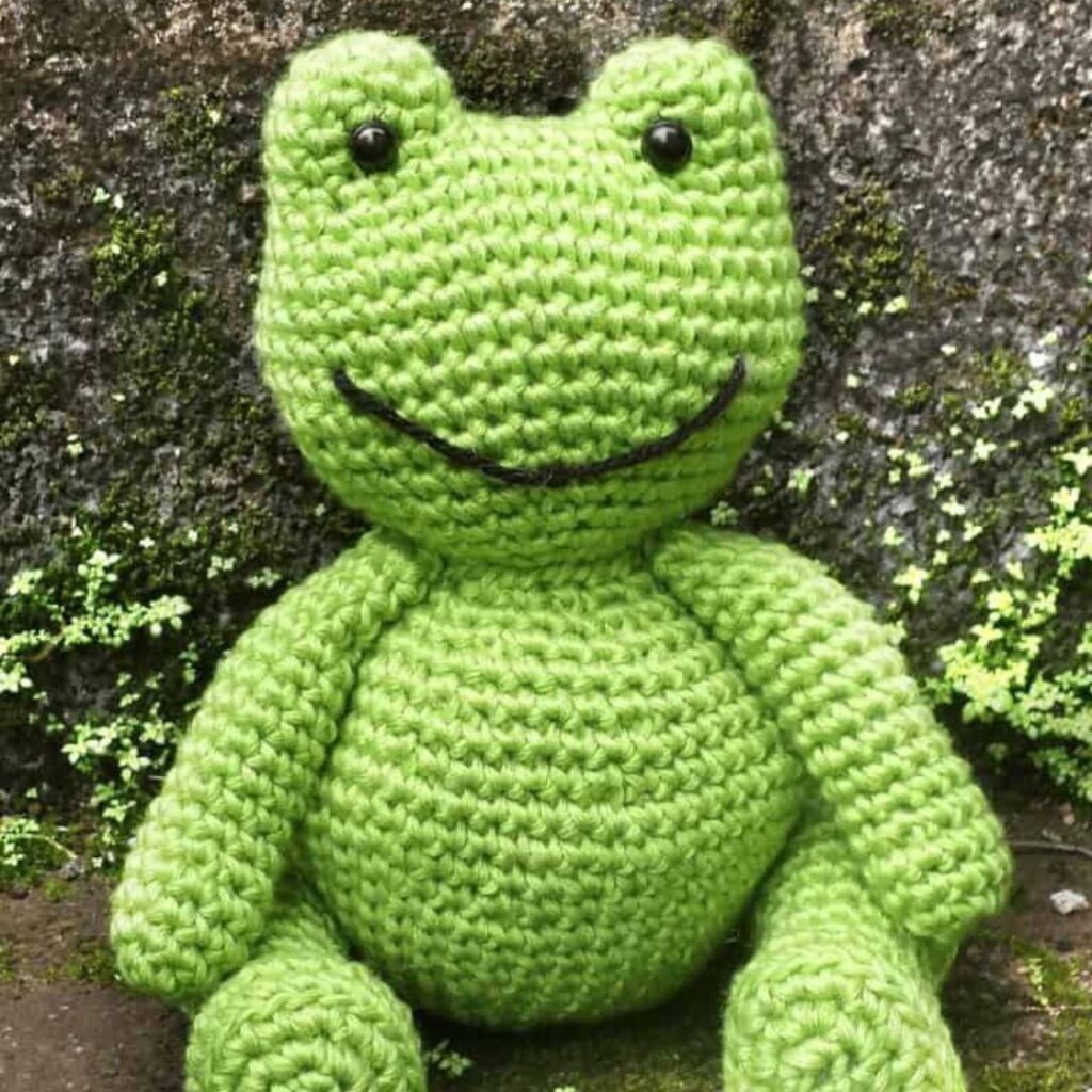 Cartoonish green crocheted frog with an embroidered smile.